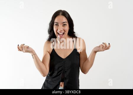 Die fröhliche junge Frau drückt mit offenen Armen und einem strahlenden Lächeln vor weißem Hintergrund pure Aufregung und Glück aus Stockfoto