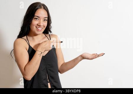 Lächelnde junge Frau, die zeigt und zeigt mit geöffneter Handfläche auf weißem Hintergrund Stockfoto