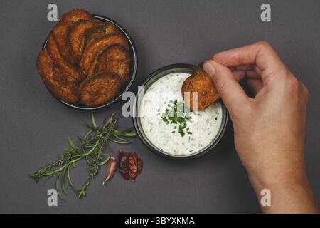 Arial Ansicht Essen würzige süße Kartoffelchips garniert mit Chili, Rosmarin und Thymian und Joghurt Knoblauch Schnittlauch Dip Sauce in schwarzen Schalen Stockfoto