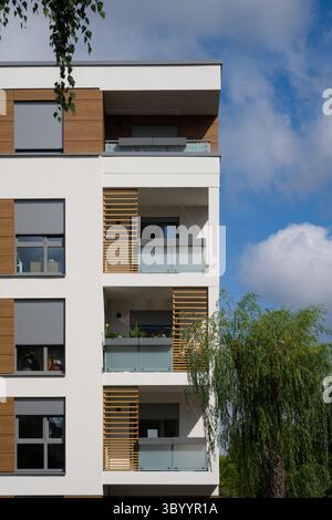 Außenecke eines modernen Wohngebäudes an einem sonnigen Tag. Die Fassade verfügt über eine Kombination aus weißen Wänden, dekorativen Holzpaneelen, Stockfoto