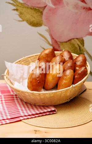 Ein Korb mit goldbraunen gebackenen Brötchen wird auf ein rotes kariertes Tuch gelegt und bietet eine warme und appetitliche Präsentation. Stockfoto