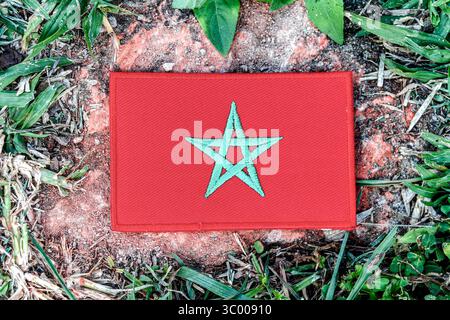 Marokkanische Flagge im Öko-Stil aus Faden, zentriert auf einem alten Felsen mit grünem Rand. Ideal für den Tag der Erde, Klimaprobleme und umweltfreundliche Reisebilder. Stockfoto