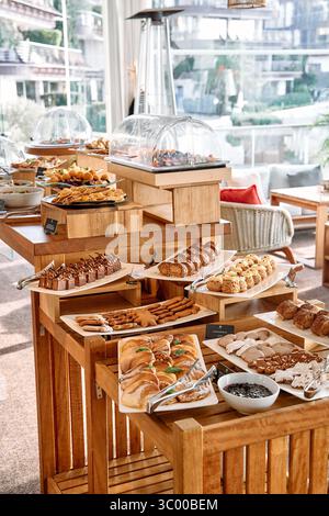 Das reichhaltige Frühstücksbuffet in einem hellen Restaurant bietet eine große Auswahl an Gebäck, herzhaften Gerichten und Backwaren, die kunstvoll auf Holztisch angeordnet sind Stockfoto