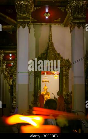 Buddhistischer Kerzenschein-Prozession in Thailand. Mönche und Gläubige spazieren an der goldenen Buddha-Statue im Tempel vorbei, leuchtende Kerzen unterstreichen die Szene. Stockfoto