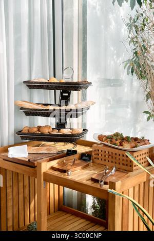 Ein elegantes und rustikales Büfett mit einer Auswahl an frischem Brot und Gebäck, wunderschön auf Holzebenen angeordnet und von natürlichem Sonnenlicht beleuchtet. Stockfoto