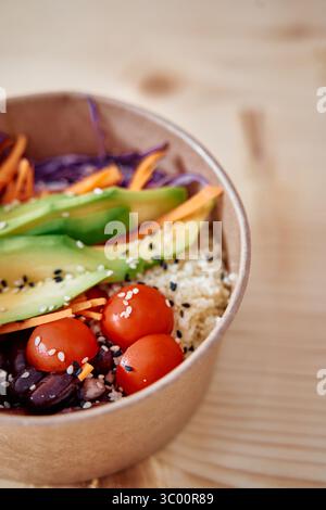 Eine lebendige vegane Schüssel mit Avocado, Kirschtomaten, Quinoa und farbenfrohem Gemüse. Diese nahrhafte Mahlzeit wird in einer braunen Schüssel auf einem hölzernen t serviert Stockfoto