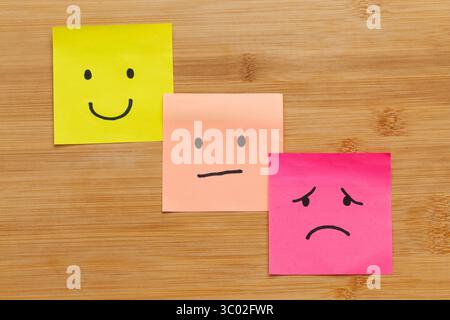 Schließen Sie drei Haftnotizen mit menschlichen Emotionen auf hölzernem Hintergrund Stockfoto