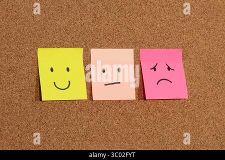 Schließen Sie drei Haftnotizen mit menschlichen Emotionen auf einem Korkhintergrund Stockfoto