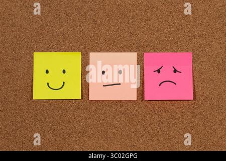 Schließen Sie drei Haftnotizen mit menschlichen Emotionen auf einem Korkhintergrund Stockfoto