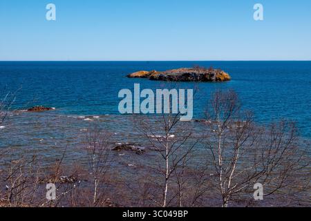 Kleine Insel an der Nordküste des wunderschönen Lake Superior in Minnesota, mit blauem Himmel und Wasser und blattlosen Bäumen an einem sonnigen Frühlingstag. Stockfoto