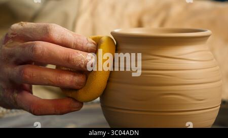 Schließen Sie sich Meister Mann Handwerker vorsichtig reiben Ton Schüssel Krug Vase Handwerker mit Halten nass gelb Schwamm männliche glatte Oberfläche dekorative Keramik Stockfoto
