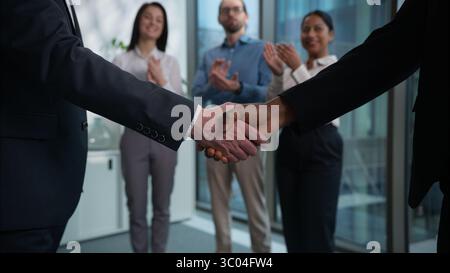 Zwei Geschäftsleute schütteln sich die Hände und schütteln den Handschlag Vereinbarung Vertrag Vertrag Kunde Direktor Erfolg Vielfalt glückliche Mitarbeiter im Hintergrund applaudieren Stockfoto