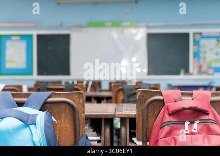 Leere Innenausstattung im Klassenzimmer mit Holztischen und -Stühlen, bunten Rucksäcken, Tafel und Whiteboard im Hintergrund. Bildungs- und Lernumfeld Stockfoto