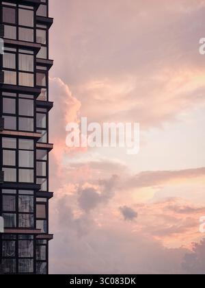 Teil des Wohngebäudes vor dem dramatischen Sonnenuntergang Himmel. Modernes Hochhaus und pfirsichfarbene Wolken im Hintergrund. Stockfoto