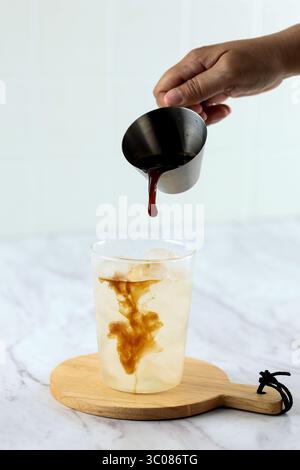 Espresso Black Coffee von Hand mit eiskaltem Kokoswasser ins Glas gießen Stockfoto