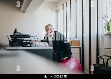 Geschäftsmann lacht beim Balancing auf einem Übungsball im Büro Stockfoto