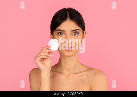 Frau, die ein Wattepad in der Nähe der Wange hält, was eine sanfte Gesichtspflege fördert Stockfoto