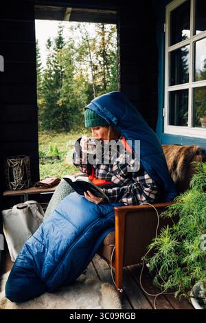 Frau, die sich im Schlafsack entspannt, liest und trinkt Tee auf cabi Stockfoto