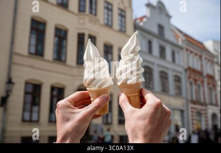 An einem sonnigen Tag halten sich zwei Vanilleeiskegel gegen historische Gebäude der Stadt Stockfoto