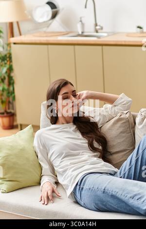 Eine junge Frau mit braunem Haar entspannt sich auf ihrer Couch und nimmt einen friedlichen Moment zu Hause. Stockfoto