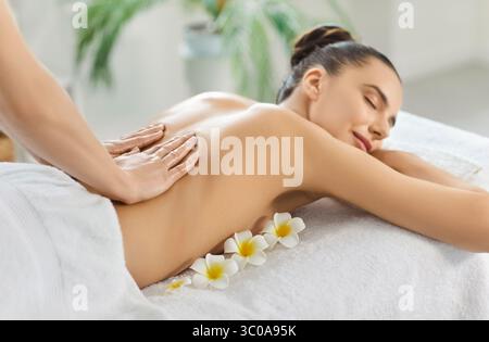 Junge Frau genießt eine entspannende, beruhigende Rückenmassage im Spa und atmet das Aroma von Blumen Stockfoto