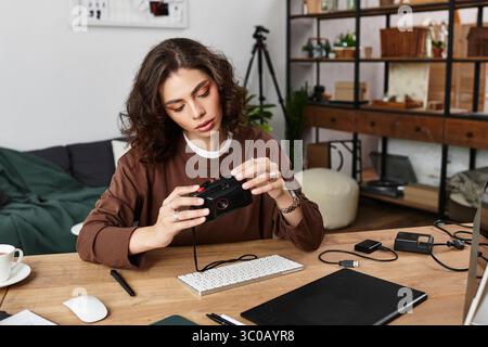 Eine junge Frau mit lockigem Haar konzentriert sich auf ihre Kamera, während sie an ihrem Schreibtisch arbeitet. Stockfoto