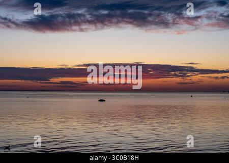 Sonnenuntergang, der dramatische Wolkenformationen von unten über dem offenen baltischen Horizont beleuchtet – lebendige Lichtphänomene, Himmelsstruktur, ruhige und poetische Atmosphäre Stockfoto