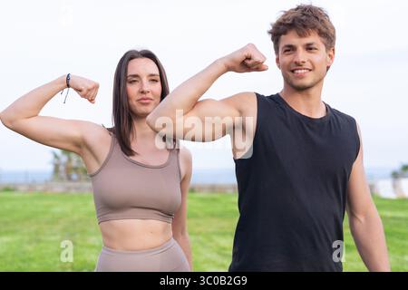 Junges Paar, das Arme biegt und lächelt während des Workouts im Park am Meer Stockfoto