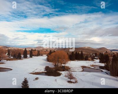 Weite Aufnahme einer Winterlandschaft, wahrscheinlich ein offener Park, bedeckt mit einer Schneedecke mit mehreren dunklen, unregelmäßigen Formen von nicht gefrorenen Wasserteichen. Stockfoto