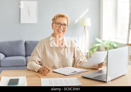 Glückliche lächelnde, reife Geschäftsfrau arbeitet am Laptop im Büro, lächelt, genießt die Online-App Stockfoto