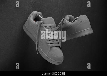 Draufsicht eines Paar stylischer grauer Sneakers mit matter Textur und perforierten Details, schräg auf einem dunklen Steinhintergrund platziert. Die Schuhe enthalten Stockfoto
