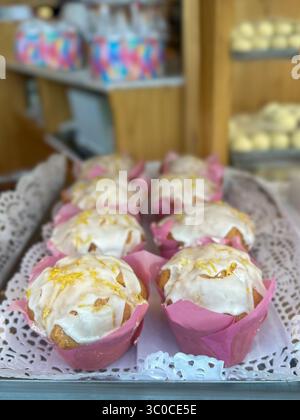 Frisch gebackene Muffins in rosafarbenen Cupcake-Einlagen, andere Backwaren sind im Hintergrund verschwommen. Die warmen Töne und der weiche Fokus deuten auf eine gemütliche Atmosphäre hin Stockfoto