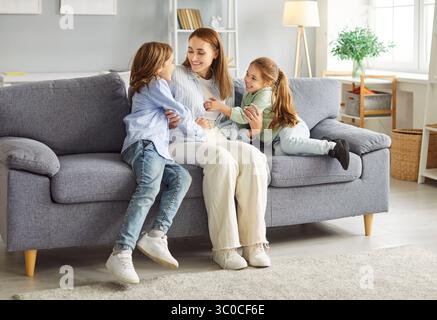 Mutter verbringt Zeit mit ihren Kindern auf der grauen Couch im Wohnzimmer, hat Spaß und lacht zusammen. Stockfoto