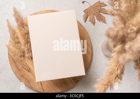 Leere Hochzeitseinladungskarte Mockup auf Holztablett mit Umschlag und trockenen Pflanzen, Platz für Text. Herbstneutrales Design für Grußkarte, Boho beige Stockfoto
