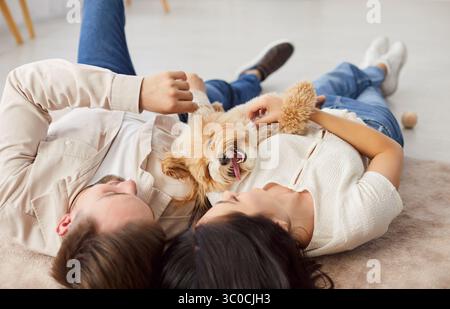 Junges Paar, das sich mit ihrem glücklichen Hund auf dem Boden entspannt und die gemeinsame Freizeit in einem gemütlichen Zuhause genießt. Stockfoto