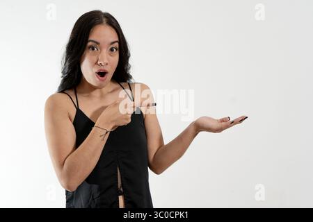 Junge Frau mit überraschtem Ausdruck, der mit der Hand auf weißem Hintergrund zeigt und zeigt, ideal für Werbe- und Marketingkampagnen Stockfoto