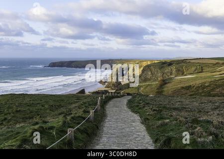 Blick auf die zerklüftete kornische Küste mit goldenen Klippen, die auf das türkisfarbene Meer treffen, ein Steinweg, der zur dramatischen Küste führt, Wadebridge, England, Großbritannien. Stockfoto