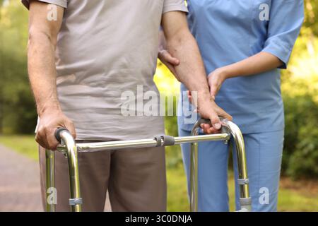 Krankenschwester hilft älteren Männern, die im Freien einen Gehrahmen benutzen, Nahaufnahme Stockfoto