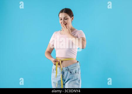 Schöne Frau mit Maßband, die alte Jeans nach Gewichtsverlust auf hellblauem Hintergrund trägt Stockfoto