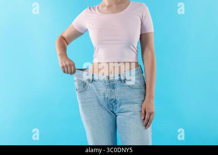 Frau trägt alte Jeans nach Gewichtsverlust auf hellblauem Hintergrund, Nahaufnahme Stockfoto