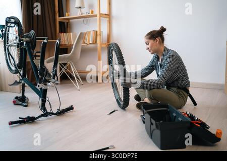 Junge Frau, die ein Fahrrad untersucht, während sie zu Hause Fahrrad repariert Stockfoto