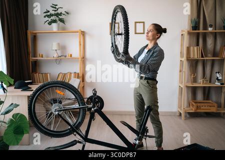 Eine junge Frau repariert ihr Fahrrad im Wohnzimmer zu Hause Stockfoto