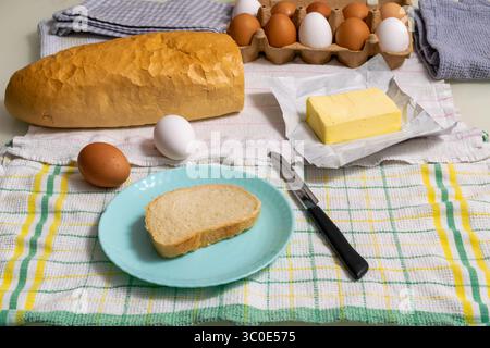 Frühstück mit gekochten Eiern und Butter, einer Scheibe Brot auf einem blauen Teller Stockfoto