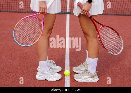 Zwei Tennisspielerinnen in Sportbekleidung mit Schlägern und Ball auf dem Platz, bereit für Match- und Teamarbeit Stockfoto