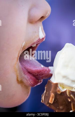 Nahaufnahme eines Kindes, das an einem sonnigen Sommertag ein Eis genießen, mit schmelzendem Vanilleeis und einem blauen Hintergrund Stockfoto