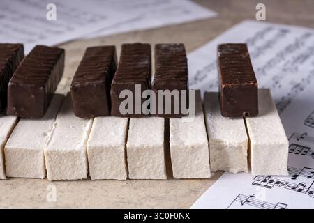 Klaviertastatur aus weißem Marshmallow und Schokolade liegt auf Notenpapier, selektiver Fokus Stockfoto