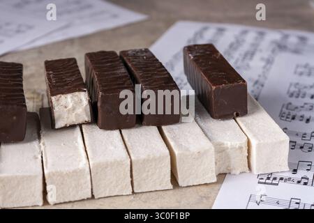 Eine Klaviertastatur aus weißem und Schokoladenmarshmallow liegt auf beigefarbenem Hintergrund, selektiver Fokus, Nahaufnahme Stockfoto