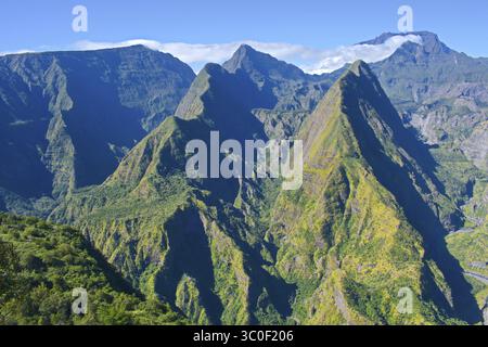 Sonnendurchflutete Berggipfel mit üppigem Grün vor einem klaren blauen Himmel, La Réunion, Frankreich Stockfoto