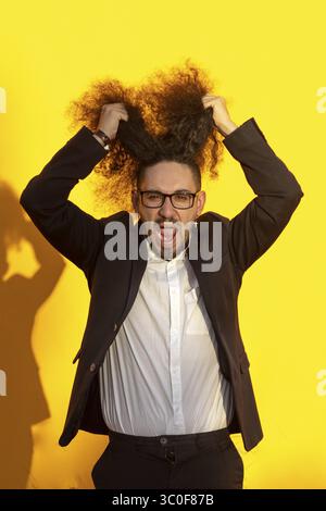 Porträt eines gestressten langhaarigen Geschäftsmannes, der sein Haar über gelbem Hintergrund rauszieht Stockfoto