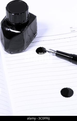 Klassischer schwarzer Füllfederhalter auf offenem Notizbuch mit Tintenflasche mit Fleck auf Seite, Blaufilter Stockfoto
